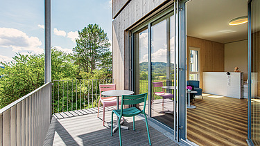 Außenansicht eines Zimmers mit Balkon und Sitzgelegenheit und Blick in den Innenraum