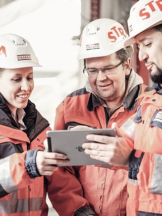 Foto Drei Personen mit Helm schauen auf ein Tablet