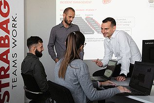 Foto Vier Personen im Büro ein Mann sitzt auf dem Schreibtisch