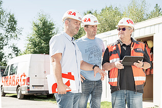 Photo Three men with helmets stand in front of a Strabag car