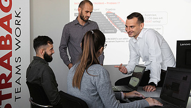 Foto Vier Personen im Büro ein Mann sitzt auf dem Schreibtisch