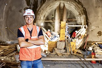 Bauleiter Florian Fuchs steht mit Kladde und Helm auf einer Baustelle