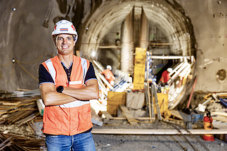 Site manager Florian Fuchs stands on a construction site with a pad and helmet