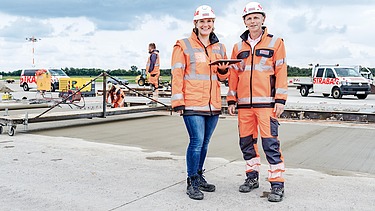 Zwei Kolleg:innen stehen zusammen auf der Baustelle