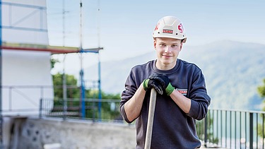 Foto: Ein Lehrling stützt sich auf eine Schaufel und blickt in die Kamera