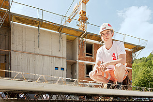 Foto: Ein Lehrling sitzt in der Hocke auf einem Rohbauelement und blickt in die Kamera