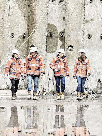 Photo Four employees with protective clothing in front of concrete wall