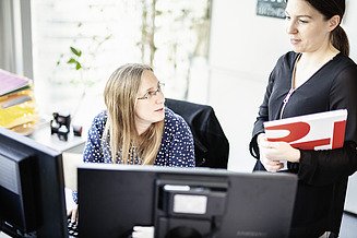 Foto Zwei Mitarbeiterinnen besprechen sich vor zwei Bildschirmen